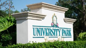 White stone sign says University Park Country Club with shrubs in front of it