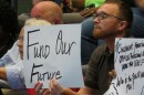 A man holds a sign that reads "Fund Our Future" at a Cincinnati School Board meeting. 
