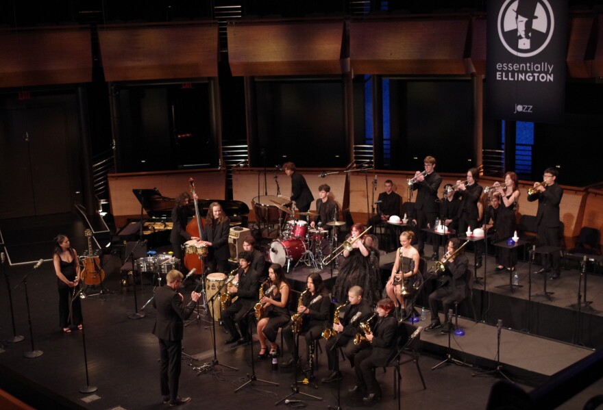 Student musicians dressed in black on a stage with an "Essentially Ellington" sign in the background.