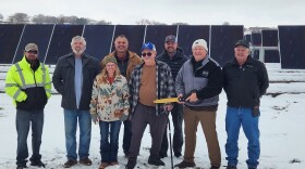 Delta City Manager Elyse Casselberry (front row left); Delta City Mayor Kevin Carlson (front row with scissors) and City of Delta Municipal Light & Power Manager Adam Suppes (third from the left, second row) are flanked by council members and employees during the Grand Opening of the Solar Array on Kellogg Street.