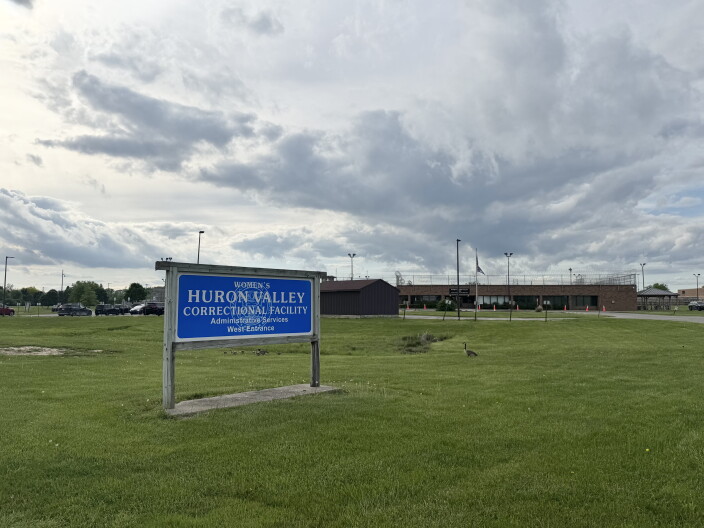 A sign outside a prison that says "Women's Huron Valley Correctional Facility" in white text on a blue board.