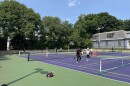About a dozen people playing pickleball on the South Street Courts in Jamaica Plains, Boston. It's a sunny day and trees line the court. 