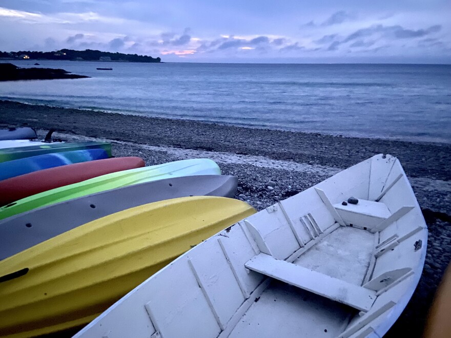 Dory and colorful kayaks on a beach at dusk