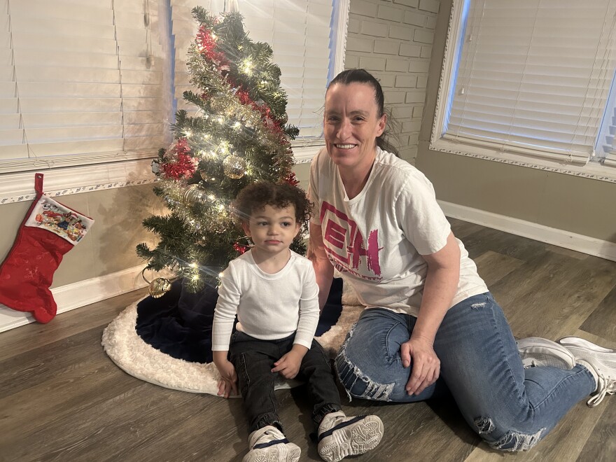 Kerry Stock sits in front of small Christmas tree with grandson Braylon