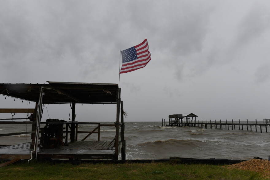 An American flag flaps in the wind generated by the effects of Isaias on an empty beach on Friday, Oct. 9, loom overhead on Friday, Oct. 9, 2026, in Mon Louis Island, Ala.