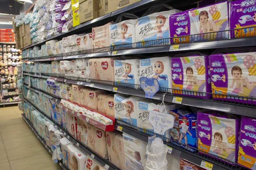 The image shows a store aisle where the shelves are filled with different brands of diapers.