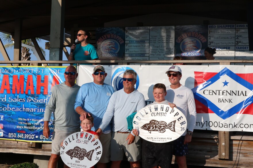 Group of men stand with their plaques that denote them as having caught the largest fish in the tournament for the youth division and overall