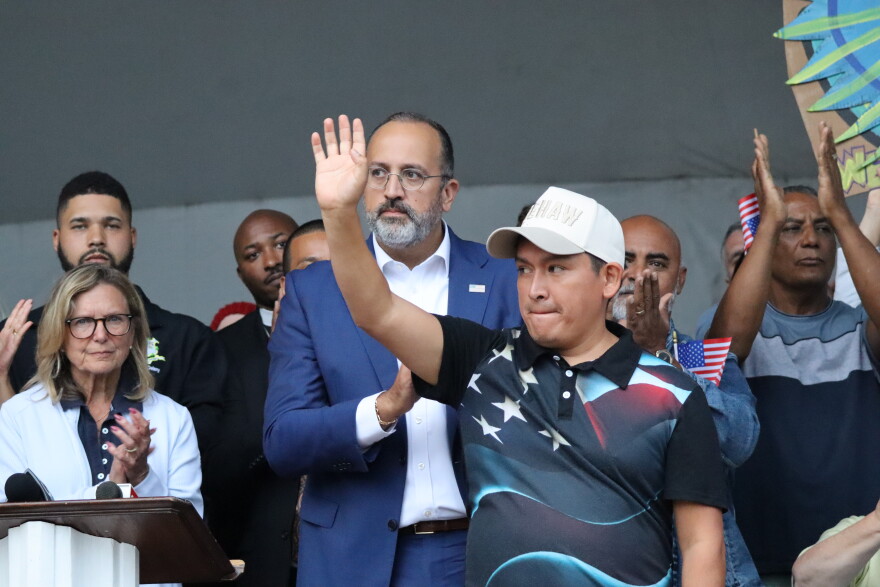 Luis waves to a crowd as Danbury Mayor Roberto Alves stands behind him.