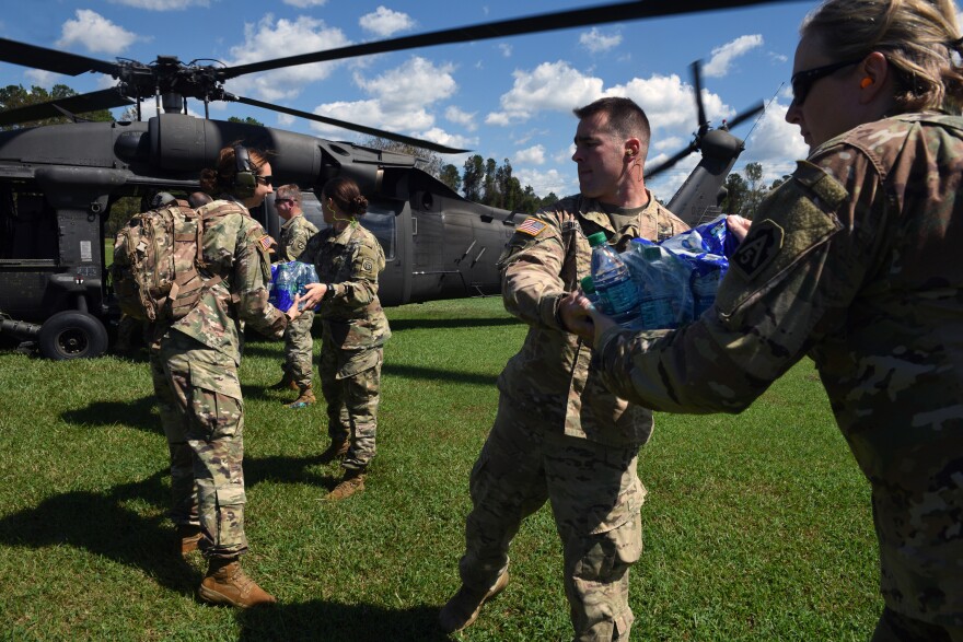 U.S. Army servicemen and women distribute water bottles and supplies.