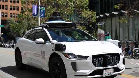 A Waymo stops at a light in San Francisco, the photo is taken from the front of the car so you can see that there is no driver, and that the car has cameras on all sides 