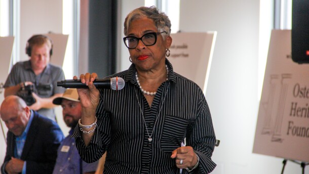 An older Black woman in a suit holds a microphone. 
