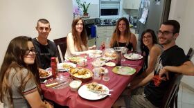 A family of six sits around the dinner table in their home, posing for the camera.