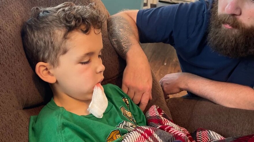 Jonah Reynolds sits with his father in May 2022 after a doctor extracted a tooth that had caused Jonah severe pain.