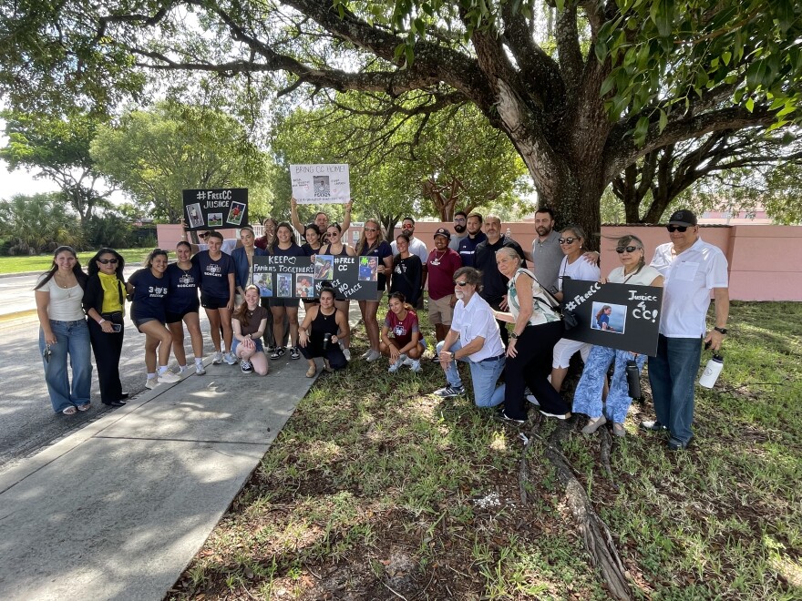 A crowd gathers for a group photo, some are holding sings calling for the release of Claudia Carolina Rodriguez Caglianone from ICE custody