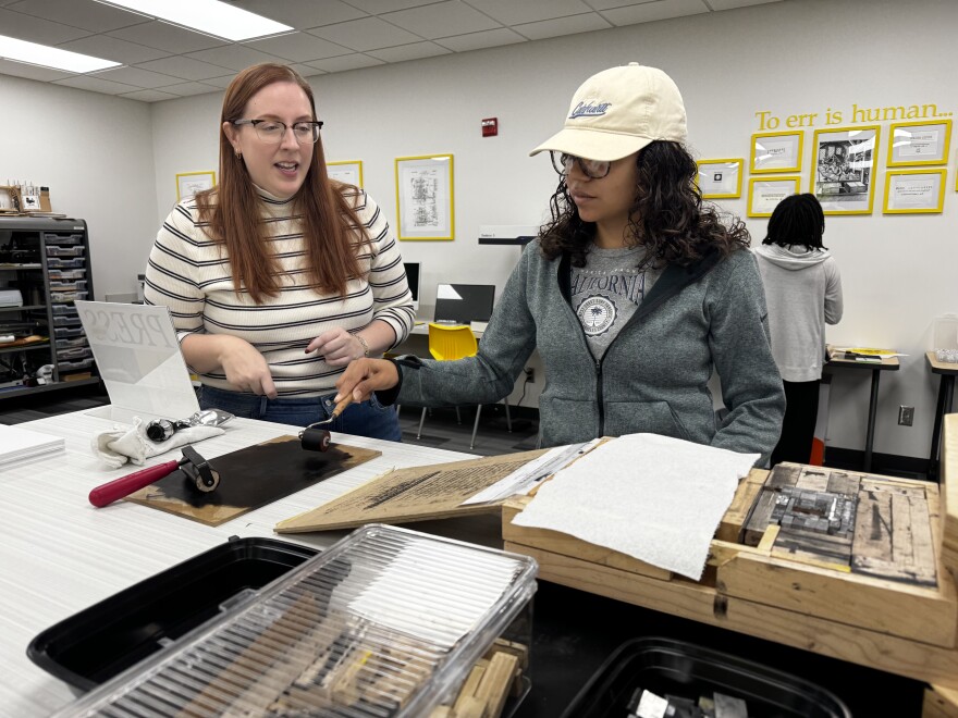 Katie Lanning, an associate professor of English at Wichita State University, helps a student use a Book Beetle machine, which mimics a full-size Gutenberg press. A new Book Technologies Lab at WSU was funded by a donation from Lanning's family in honor of her late grandfather, Robert L. Cattoi.