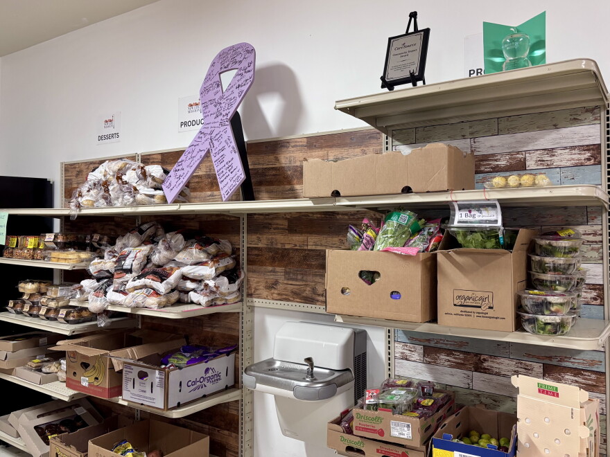Boxes of vegetables and berries, bags of potatoes and containers of bakery items sit on shelves in a lit room.