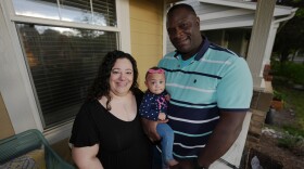 A man and woman hold a small child outside a home.