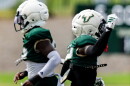 two football players pass each other running in different directions, both wearing dark green jerseys and white helmets 
