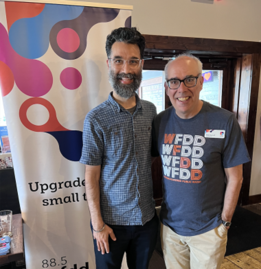 Neal Charnoff and a listener at a bar meetup standing in front of a WFDD banner