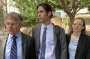 Man with dark hair wearing suit is flanked by man on left and woman on right also in suits