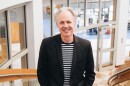 a white man with gray hair and a black jacket over a striped shirt smiles at the camera in the Monroe County Public Library