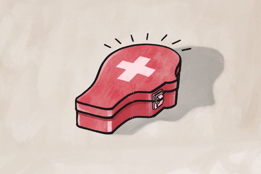 An illustration of first aid kit that is shaped like a person's head. It is red with a first aid cross symbol on it. 