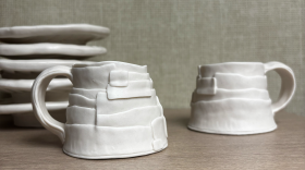Two white hand-built ceramic mugs sit on a wooden counter.