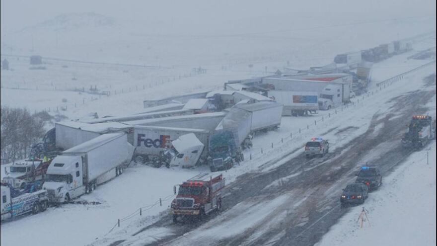  A group of semi trucks are crashed into one another on slick, snowy winter roads. There are also some emergency responder vehicles.