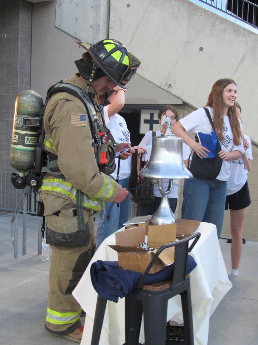 A man in a firefighter uniform rings a silver bell. 