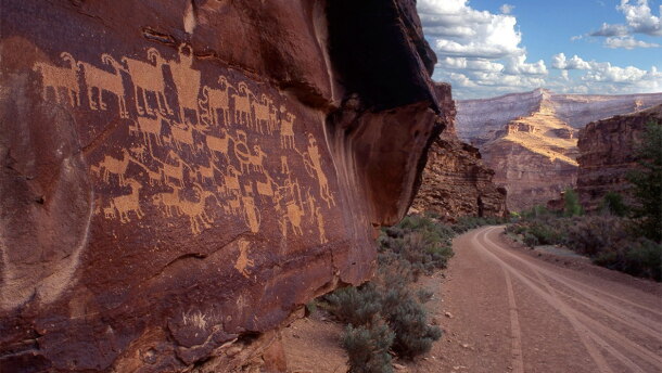 Petroglyphs of animals carved into the side of a red rock wall. 