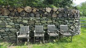 A row of chairs in front of a stone wall with logs on top of it.