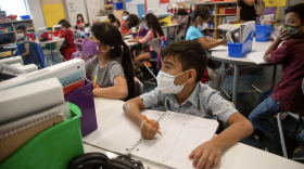 Students sit at desks in a classroom wearing masks.