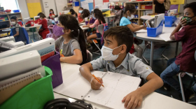 Students sit at desks in a classroom wearing masks. 