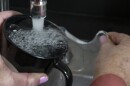 A woman's hand holds a black coffee cup beneath a faucet. Her other hand is turning the lever to run the water.