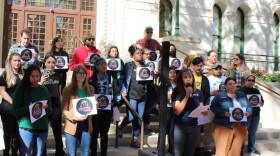 Organizers standing in front of the San Antonio Justice Charter on the steps of City Hall. Ananda Tomas, the executive director of ACT 4 SA, one of the organizations leading the push for the charter amendment, stands in front with a microphone. 