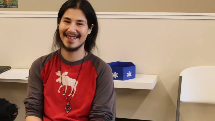 A person wearing a red long sleeved shirt near a table with a tan wall in the background