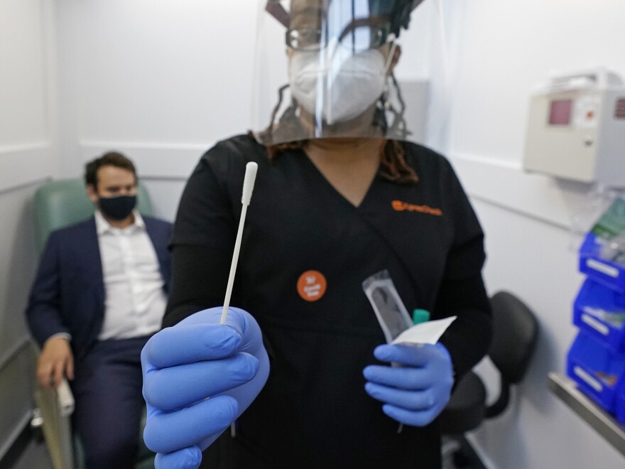 A medical assistant holds a swab after testing a man on Wednesday at the new COVID-19 testing facility at Boston Logan International Airport.