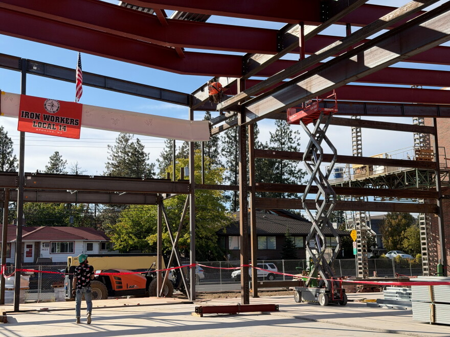 A white steel beam is lifted into place at a building under contruction.