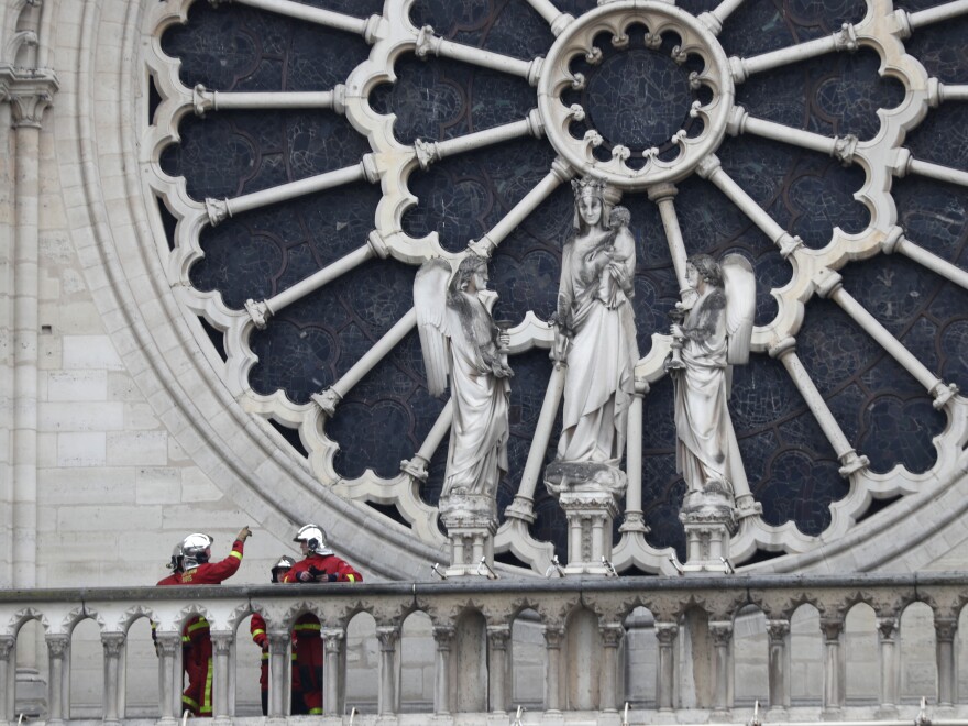 Firefighters talk near the cathedral's rose window on Tuesday. Experts are assessing the blackened shell of Paris' historic cathedral to establish next steps to save what remains.