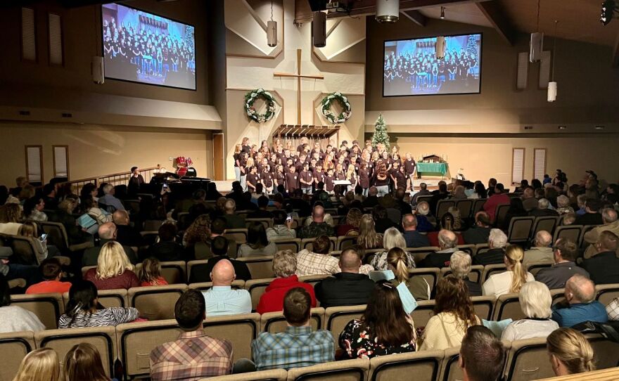 A wide shot of a church with several rows of people watching a choir in the background. 