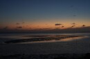 A sunset sky reflects off of water surrounding a sandbar 