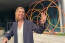 U.S. Senator Elissa Slotkin stands and smiles over her left shoulder as she waves. She's standing in front of a scultpure with yellow, orange and red circles. Behind that is a door to enter the Helen Devos Children's Hospital in Grand Rapids.