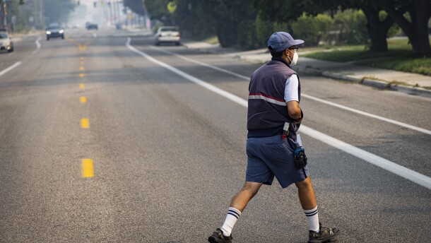 A postal worker crosses a street  as smoke from Oregon wildfires affects air quality in downtown Boise. He is wearing a N-95 mask. 