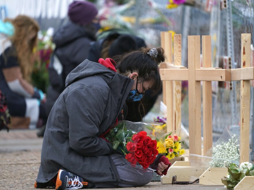 Star Samkus, who works at a King Soopers grocery store in Boulder, Colo., and knew three of the victims of a mass shooting there a day earlier, kneels in front of crosses put up for the victims outside the store on Tuesday.