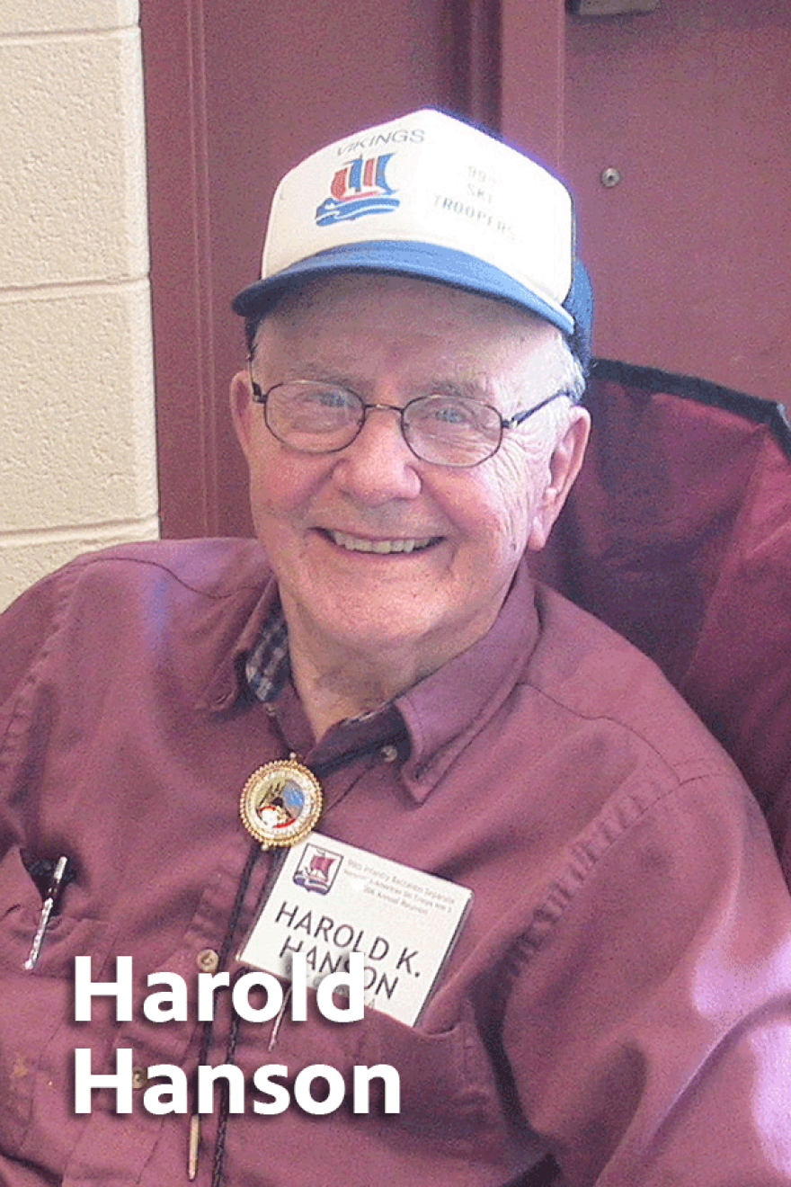 Elderly Harold K Hanson wearing glasses, a red button-up shirt and a bolo tie, and a blue and white baseball cap.