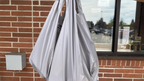 A person holds up a thick plastic bag in front of a brick wall. 