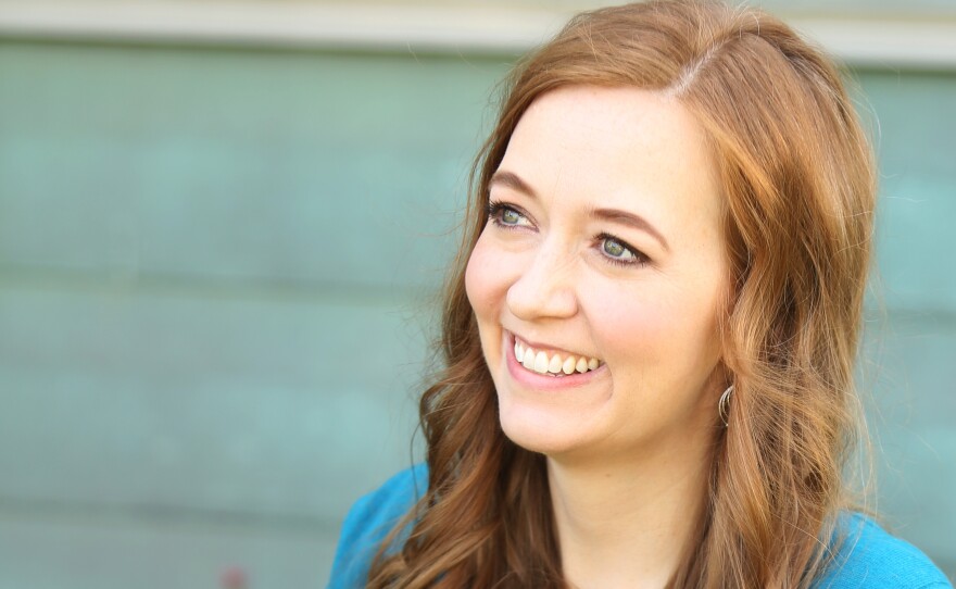 Shannon Hale, a white woman with brown hair, looks off to the side, smiling. She is wearing a blue shirt and sitting outside.