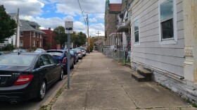Wide concrete sidewalk that extends from houses to street. cars parked along street, houses on right side