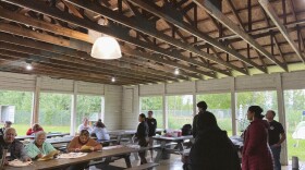 People sit at picnic tables in a high-ceilinged wooden building.