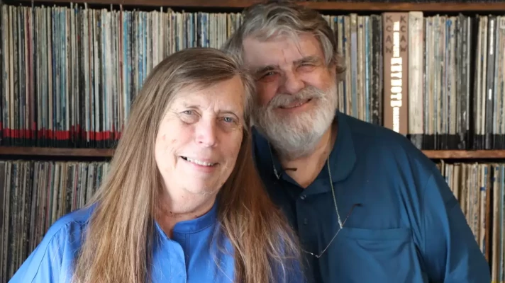 A man and a woman stand before a library of vinyl records. 